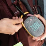 شخصی در حال بستن اسپیکر JBL Clip 4 به بند کوله‌پشتی – مناسب برای فضای باز و حمل آسان